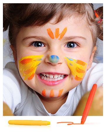 Colorful face paint applied to a child's face in yellow and orange patterns. Orange and yellow face paint crayons visible below.