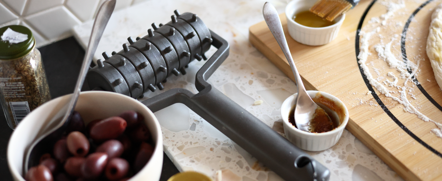 Close-up of kitchen preparation surface with olives in bowl, cooking utensils, and flour-dusted workspace.