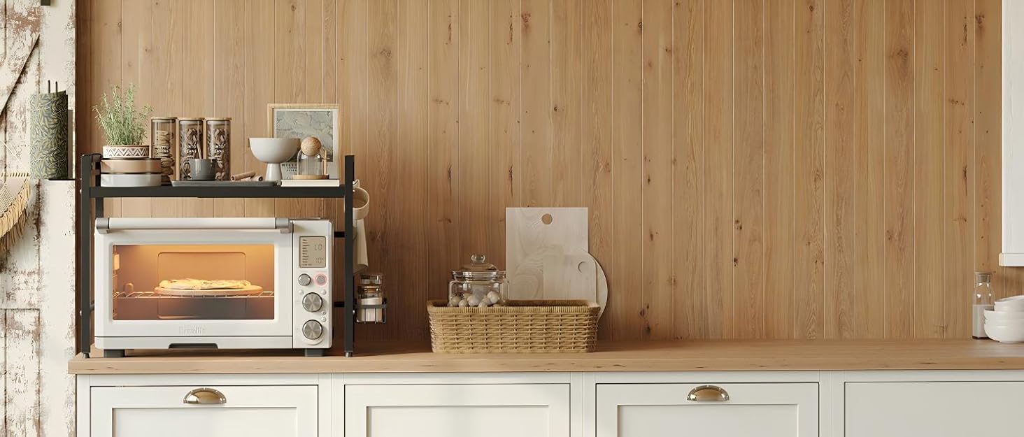 Countertop toaster oven with glass door and illuminated interior, placed on white cabinetry against wooden paneled wall. Basket and kitchen accessories visible on counter.